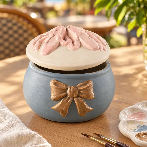 A round ceramic keepsake box with ballet slippers on the lid, painted slate blue with a bronze bow